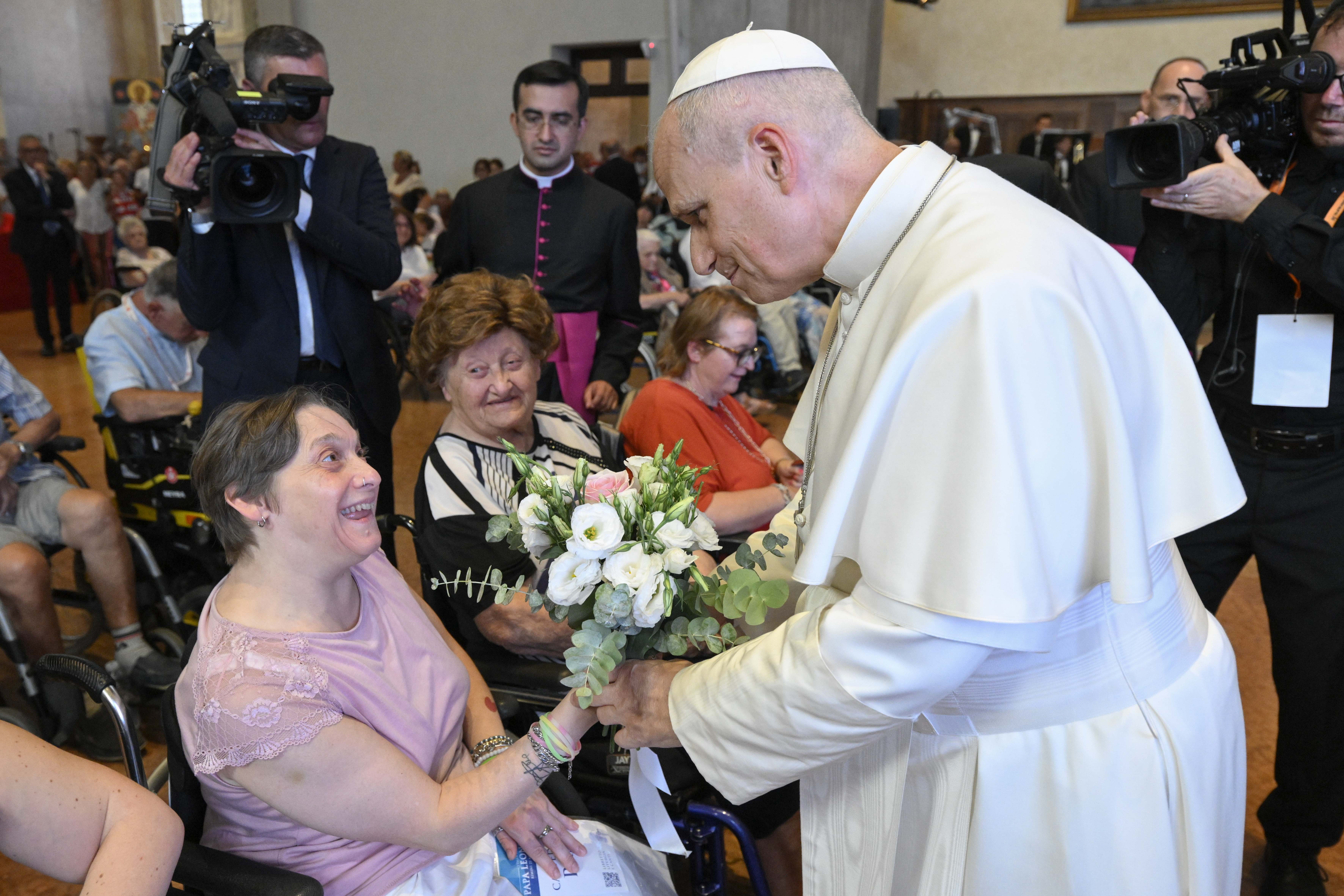 Pope Leo XIV is handed flowers by a woman in a wheelchair at Rimini Cathedral, Aug. 22, 2026, during a meeting with people suffering from illnesses and disabilities. | Credit: Vatican Media
